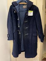 Full view navy duffle coat hanging, shows length, hood, toggles