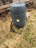 full view of gray rain barrel on metal stand with hose