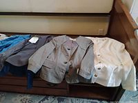 Five jackets laid out on bed: teal blue, charcoal, grey plaid, ivory, beige