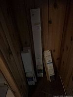 Three boxed mini blinds leaning against wood panel wall