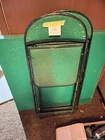 Three or more folded green and black metal chairs leaning against wall