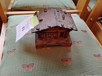 Front view showing carved chalet exterior, shuttered windows, bench, logs, roof detail