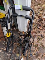 Full view of folded trunk bike rack showing frame, foam pads, yellow cradles, attached straps