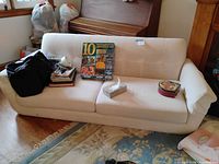 Full front view of white three-seat sofa with items on top