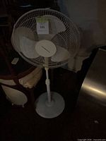 Front view of white oscillating pedestal fan showing blade guard, control housing, pole and base