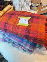 Stacked orange/red plaid and multicolour mohair throw blankets showing pattern, texture and fringe