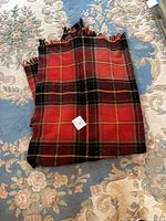 Folded red tartan wool throw showing overall pattern and fringe