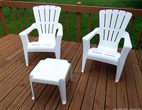 Two white plastic Adirondack chairs and matching square plastic side table on wooden deck