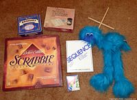 All items: Scrabble, Triple Yahtzee, Sequence, dominoes tin, Uno cards, blue furry marionette puppet with wooden control cross displayed on floor