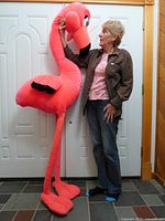 Full view of oversized pink flamingo plush held upright beside adult for scale
