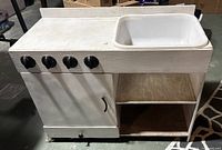 Front view of wooden play kitchen with sink basin, control knobs, cabinet door and open shelf