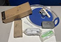 Group view of all items including can opener, glass lid, two boxed items, white scraper, grey tin, sealed green utensil