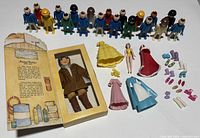 All items laid out: Playmobil figures, boxed Amelia Earhart doll, Polly Pocket figure, dresses and accessories