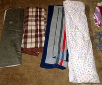Four folded textiles: olive throw, plaid blanket, striped throw, sprinkle quilt