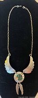 Full view of sterling silver necklace showing chain, winged pendant, medallion with green stone inlay, and feather drops