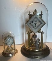 Both dome clocks side by side under glass domes