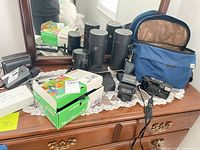 Group shot of cameras, lens cases, flashes, camera bag on dresser