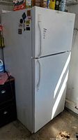 Full exterior view of white top-freezer refrigerator with magnets and wear