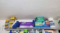 Overall view of Glad boxes, Swiffer WetJet pads box, Swiffer cloth tubs, mop head and paper towel on wire shelf