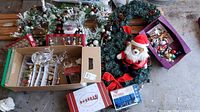 Overall lot showing wreath, garland, ornaments boxes, plush Santa dog, snow globe, acrylic deer, string lights packaging