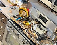 Overview of utensils piled on stove, showing variety and quantity