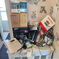 Overall lot on small cabinet showing boxed VTech system, Belkin cable packs, Shure cable box, SanDisk flash drives, loose handsets, desk phone and cables