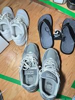 Pair of gray New Balance sneakers and tagged Reebok flip-flops shown together