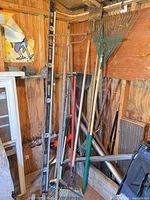 Overall view of assorted rakes, shovel and spirit levels leaning in shed corner
