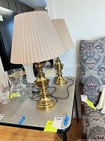 Pair of brass table lamps with pleated shades on tabletop, cords visible