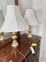 Two polished brass table lamps with white shades on dresser