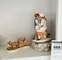 Shelf view showing both porcelain figurines: couple music box and horse carriage
