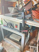 Full view of Ryobi table saw on metal stand with miter saw head and accessories stacked on top