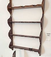Full view of wall-mounted wooden plate rack shelf showing four ledges and hooks