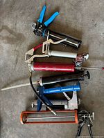 Group of grease guns and caulking gun on floor