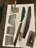 Assortment of trowels, smoothing blades and notched tools laid on white board