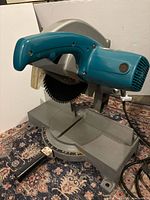 Front left view of Makita 355 mm cut-off saw showing handle, blade, base and power cord
