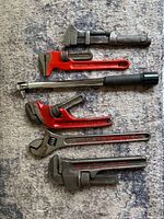 Six hand tools laid out: four pipe wrenches, one torque wrench, one adjustable wrench
