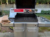 Weber Genesis BBQ open with rotisserie box across grates and cedar planks stacked on side shelf