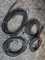 Four coiled welding cables with various plugs on gravel