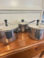 Three stainless pots with lids on wooden surface