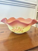Side view of pink-to-yellow ruffled glass bowl with floral painting