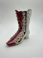 Side view of porcelain boot vase showing pink front, white rear, floral scroll, gold trim