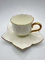 Cup on saucer front view showing gold trim and leaf shape