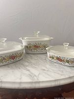Three covered casserole dishes grouped on marble surface
