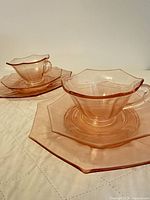 two sets of rose pink glass cup, saucer and plate