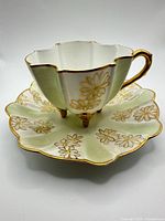 Teacup on saucer front view showing scalloped shape, pale green panels and gold floral pattern