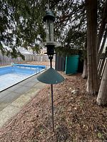 Full view of stake bird feeder with green squirrel baffle next to pool
