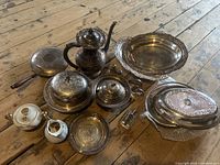 Group of tarnished silverplate serveware and two porcelain pieces displayed on wooden floor