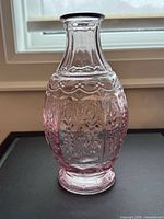 front view of pink pressed glass vase showing embossed floral motifs and fluted neck