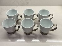Six white porcelain mugs displayed rim up